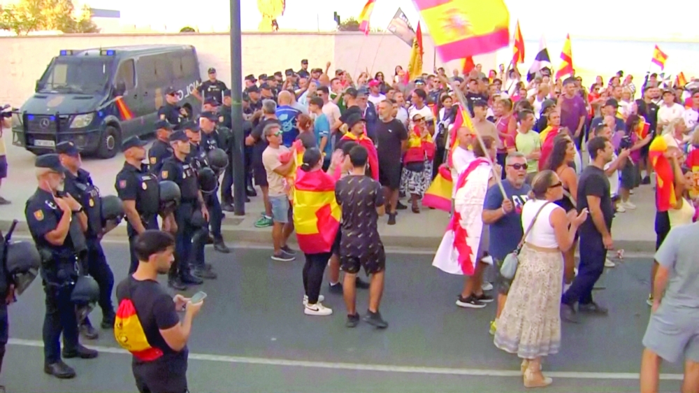Law enforcement personnel watch while protesters hold Spanish flags, as Ceuta residents destroy a migrant camp by the beach, in Ceuta, Spain. - Reuters