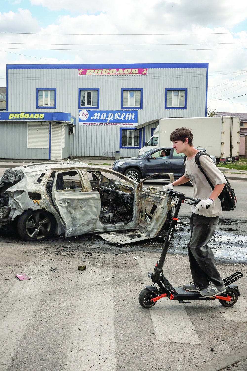A youth on a scooter passes by a burned car at the site of a Russian drone strike, amid Russia's attack on Ukraine, in Kyiv, Ukraine. - Reuters