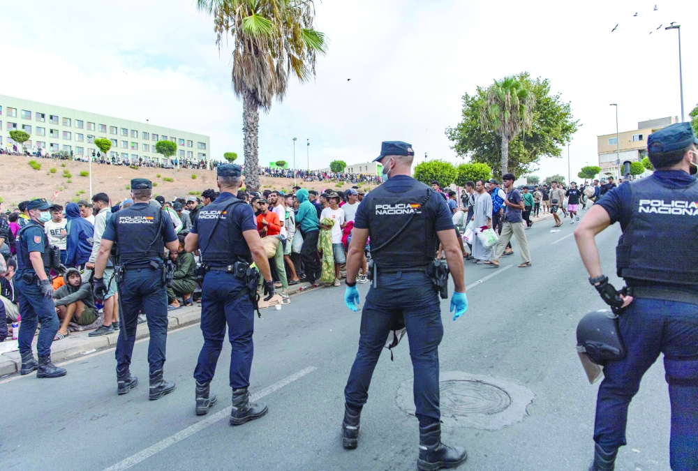 Spain's National Police officers stand as migrants wait on the sidewalk before being registered in Loma Colmenar district of Ceuta. — AFP