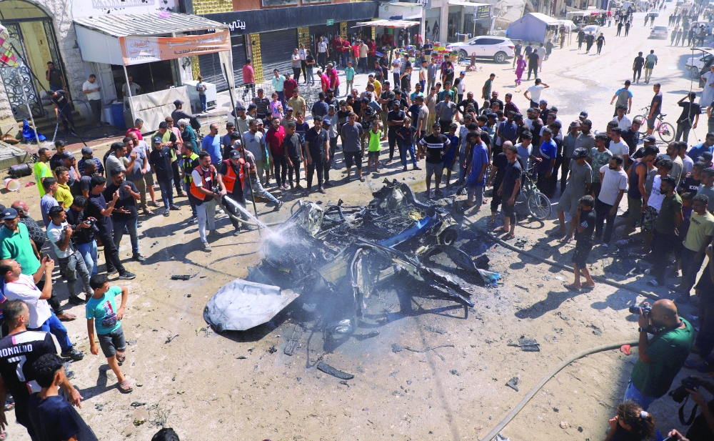 Residents gather as fire is extinguished following an Israeli air strike that hit a vehicle in Gaza City. — Reuters