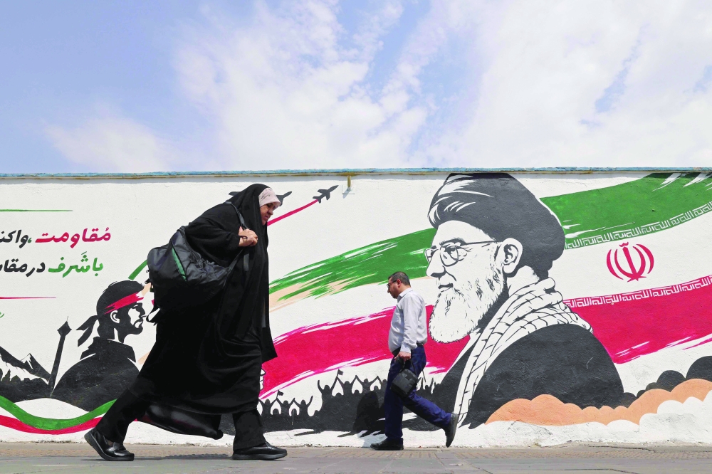 Pedestrians walk past a wall mural of Iran's slain supreme leader Ayatollah Ali Khamenei, along a street in downtown Tehran on Monday. - AFP