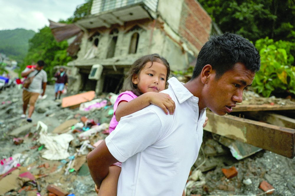 A man carries a girl next to damaged buildings following the deadly flash floods and mudslides in Nuwakot district, Nepal. - Reuters