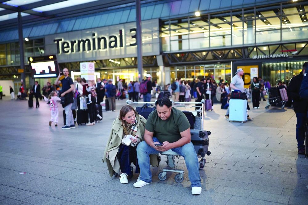 Passengers sit with their luggage outside Terminal 3 of London Heathrow airport, west of London. — AFP