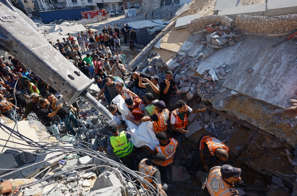 Rescuers recover the body of a Palestinian from under the rubble of a residential building that had been damaged in an earlier Israeli strike during the war and collapsed on Wednesday, in Gaza City