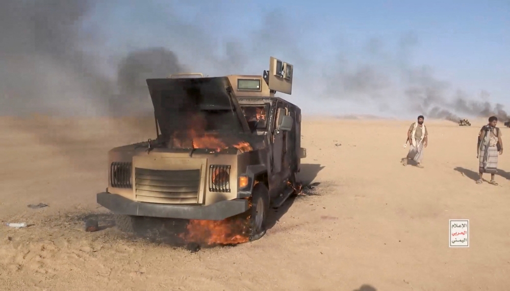 Iran-aligned Houthi fighters move next to a destroyed vehicle following what the source described as an attack on Saudi-backed forces in the location given by the source as al Jawf governorate,