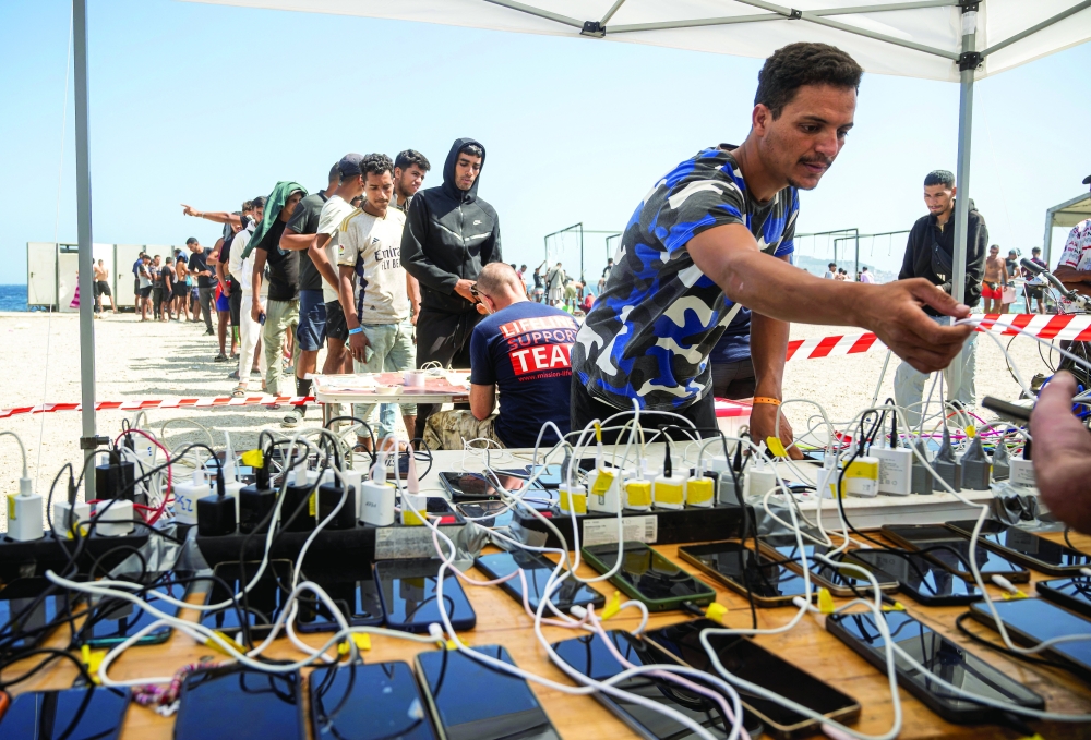 Migrants line up to charge their mobile phones with the help of an international support network called Team Lifeline near the Trampolin beach in Ceuta, Spain. — Reuters
