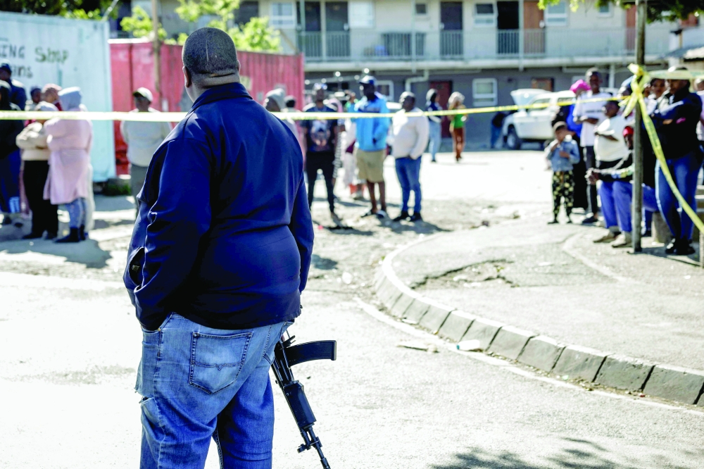 A member of the South African Police Service (SAPS) stands guard as bystanders look on behind police tape near an entertainment venue. — AFP