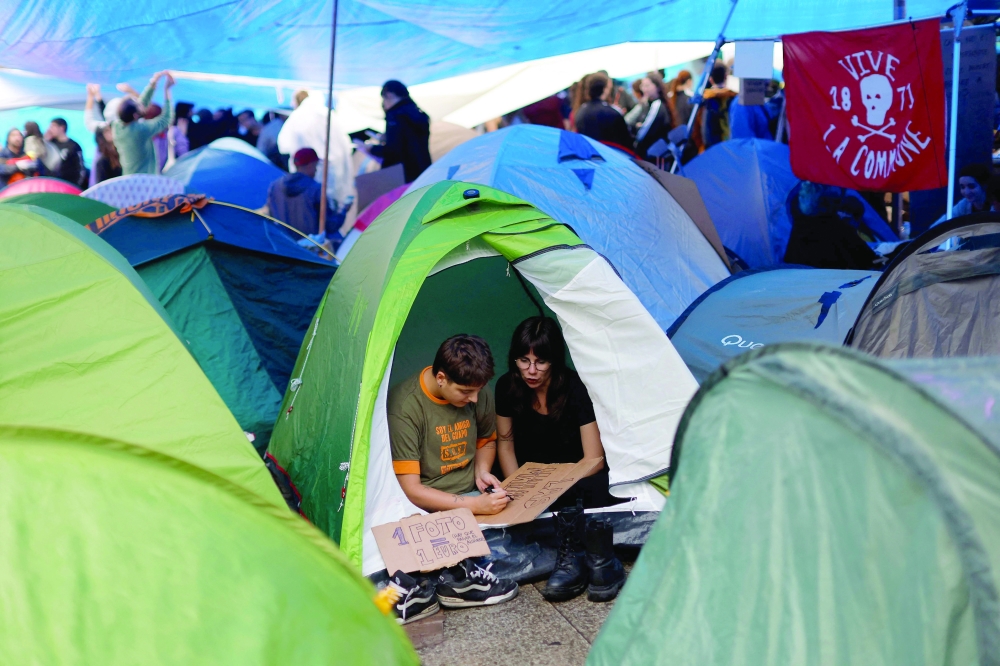 Demonstrators make banners in a tent in a camp set to protest against evictions and the housing crisis in Madrid. — AFP