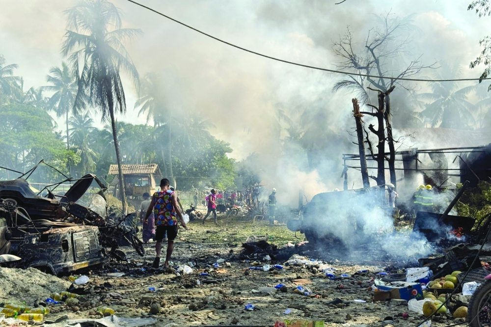 People walk through smoke and smouldering debris following a military air strike in Kyauktaw. — AFP