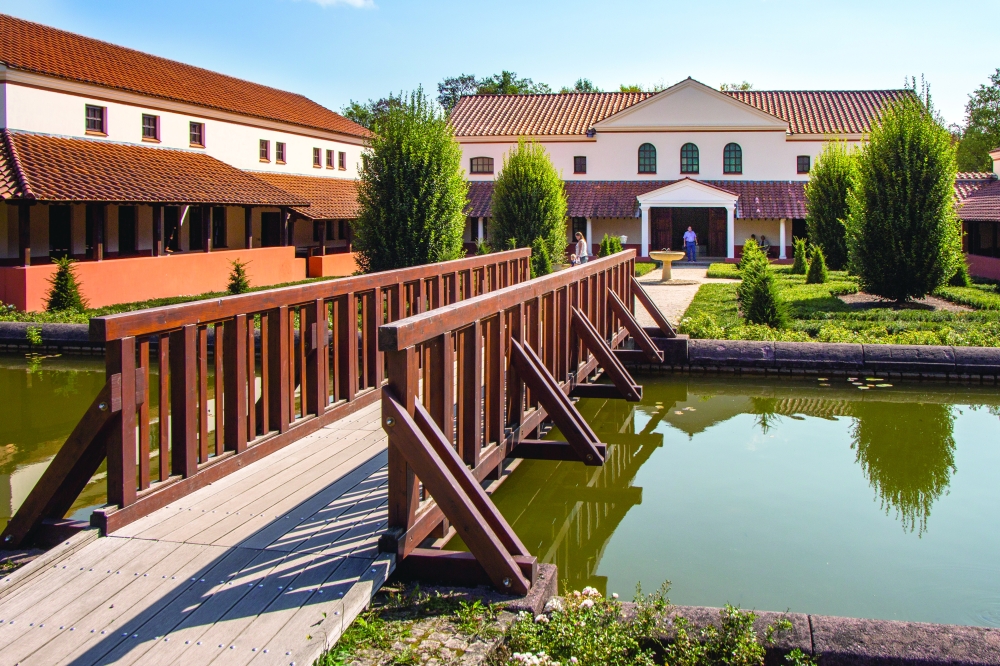 A wooden bridge leads visitors through the serene grounds of the Roman Villa Borg.
