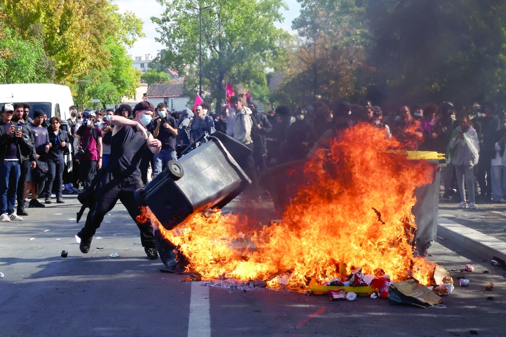 A masked protester throws a garbage bin into a fire set up in Saint-Denis near Paris, France.— Reuters