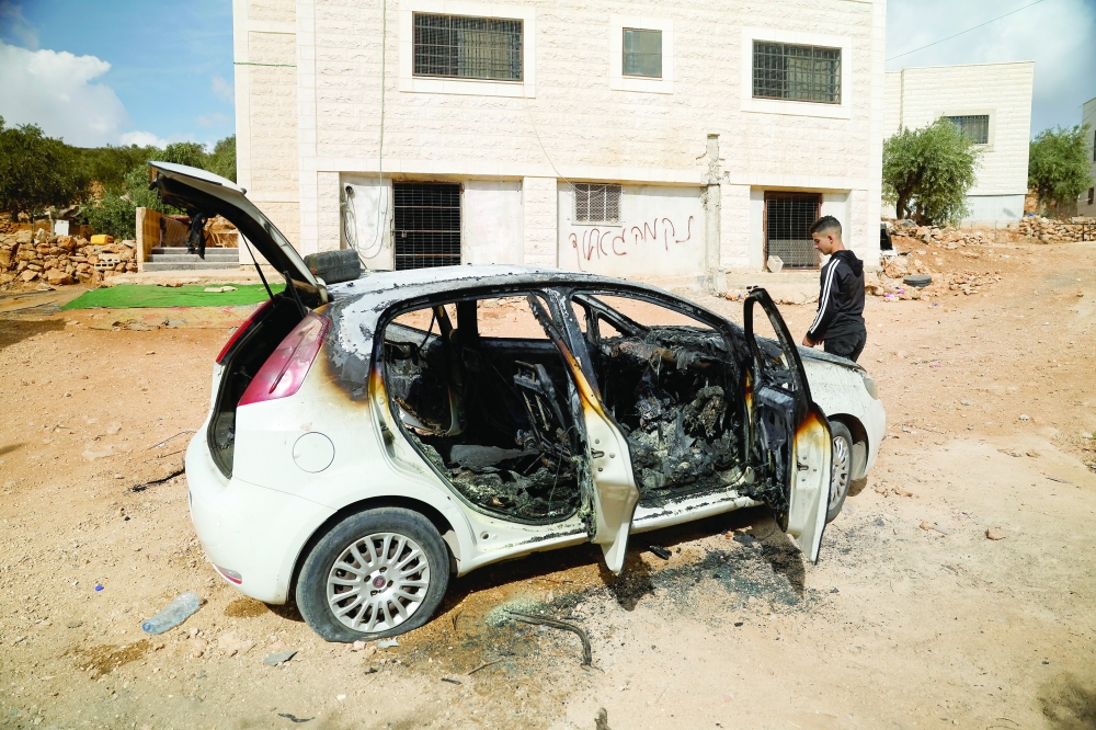 A Palestinian man walks past a damaged vehicle  in Al-Mughayyir, near Ramallah, in the Israeli-occupied West Bank. —Reuters