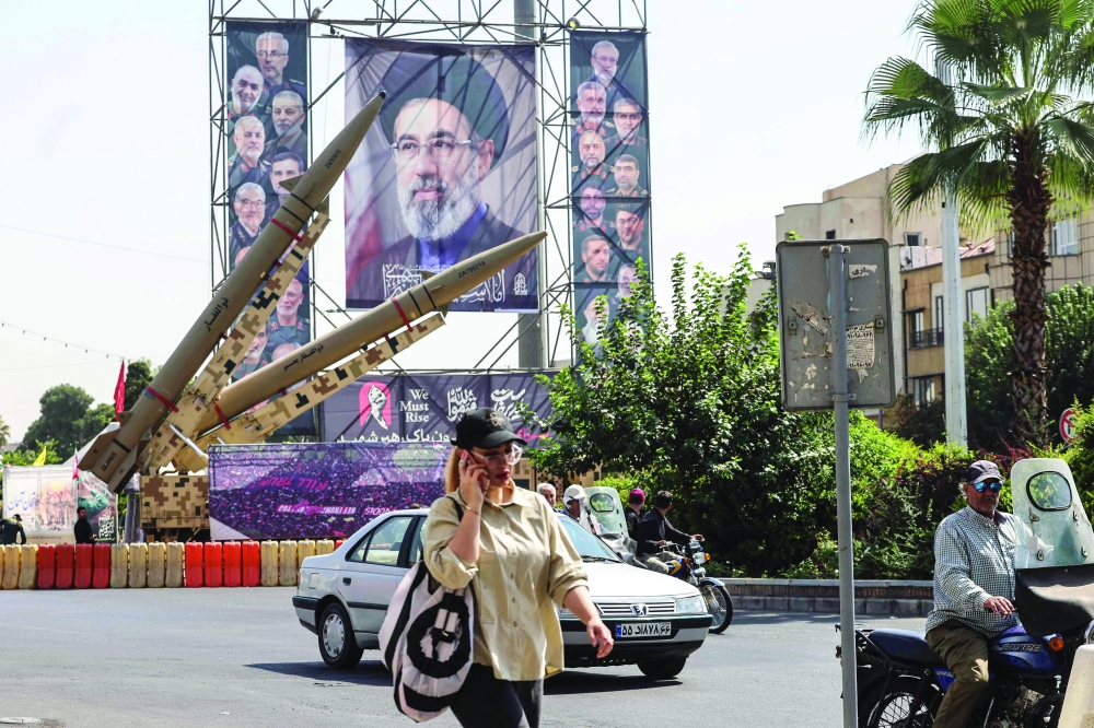 
A woman walks past Iranian-made Zolfaghar missiles on display beside a large portrait of Iran’s supreme leader Mojtaba Khamenei at Baharestan Square in Tehran. — AFP 