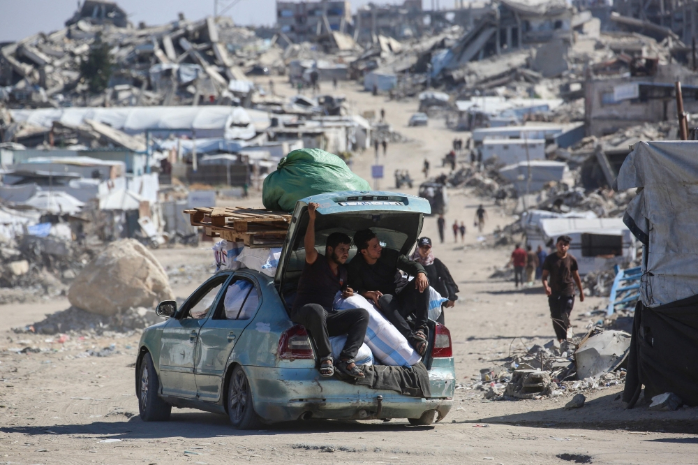 Palestinians drive a car loaded with belongings along a street lined with destroyed buildings and makeshift shelters at the Jabalia refugee camp in the northern Gaza Strip on October 5, 2026.