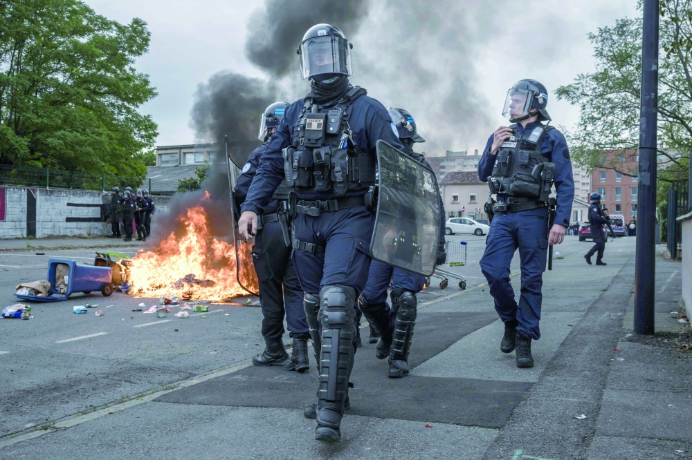 Riot police officers walk past burning trash as protesters and students gather outside the Lycee Toulouse Lautrec. — AFP