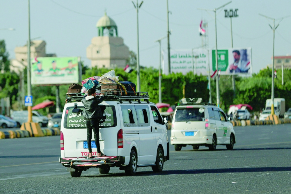 A man rides on the back of a microbus as it drives along a street in Sanaa. — AFP