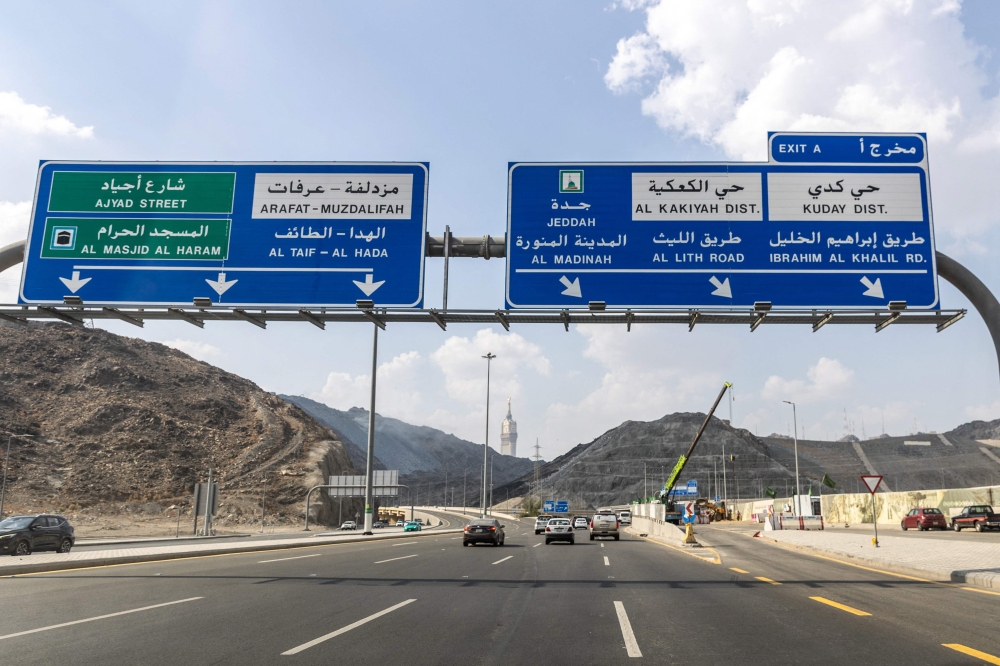 Vehicles travel along a road beneath directional signs in Mecca