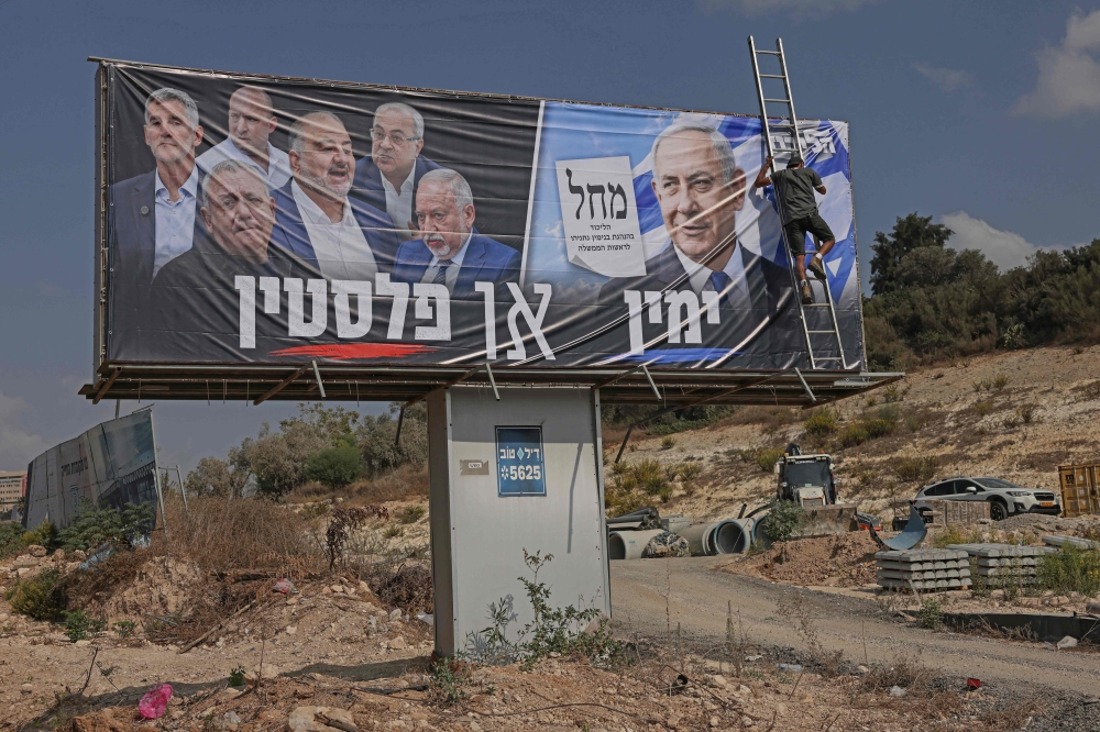 This photo taken on October 21, 2026 shows a worker unfurling on electoral campaign billboard for Israel's Prime Minister Benjamin Netanyahu's Likud party, with a Hebrew phrase reading "the Right or Palestine" alongside the faces of the members of the opposition, in Israel's northern city of Nazareth
