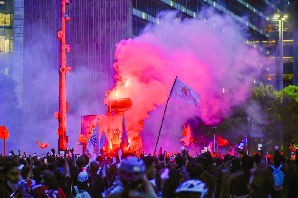 Protesters ignite a flare and wave flags during a demonstration against economic hardship