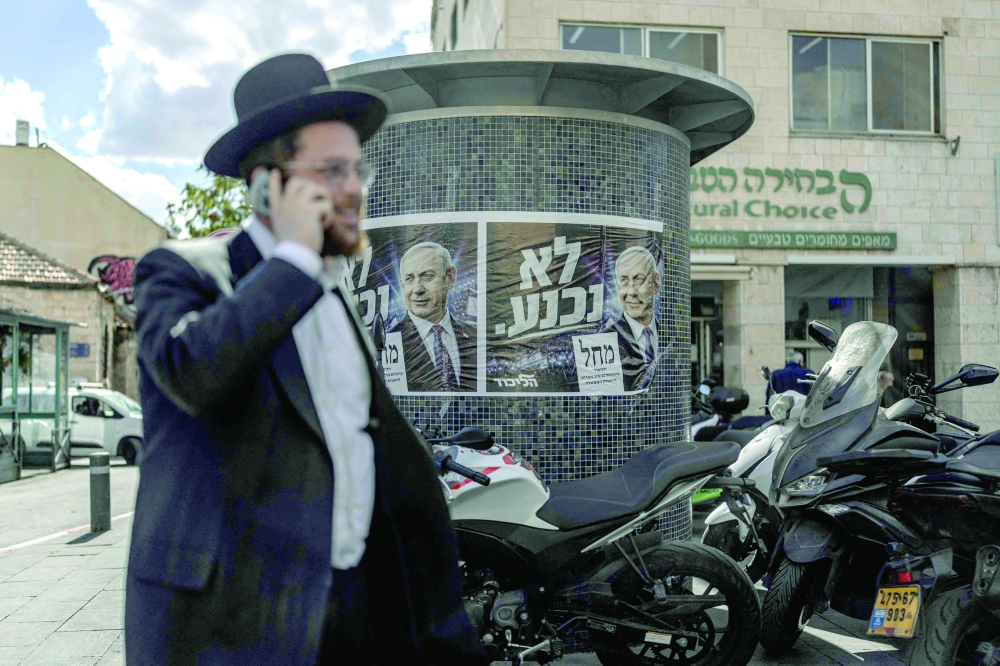 Israelis walk past a poster of Prime Minister Benjamin Netanyahu on Thursday as the country awaits the final results of the general election. — AFP