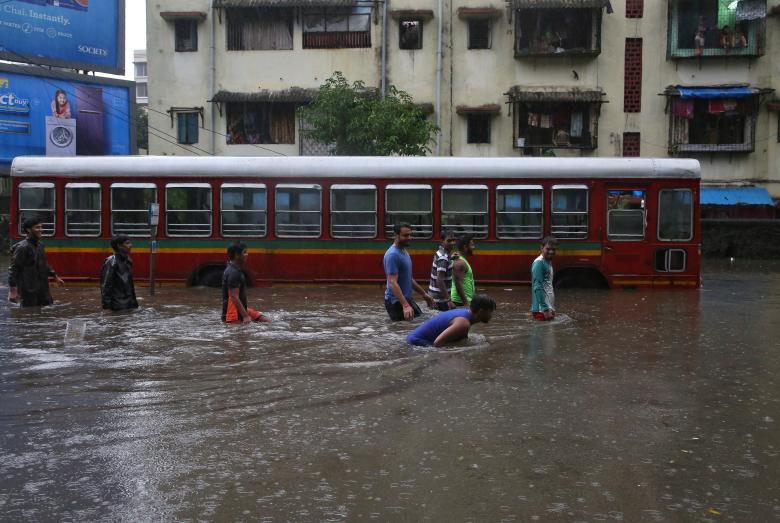 People wade through a water-logged road past a stalled passenger bus during rains in Mumbai,