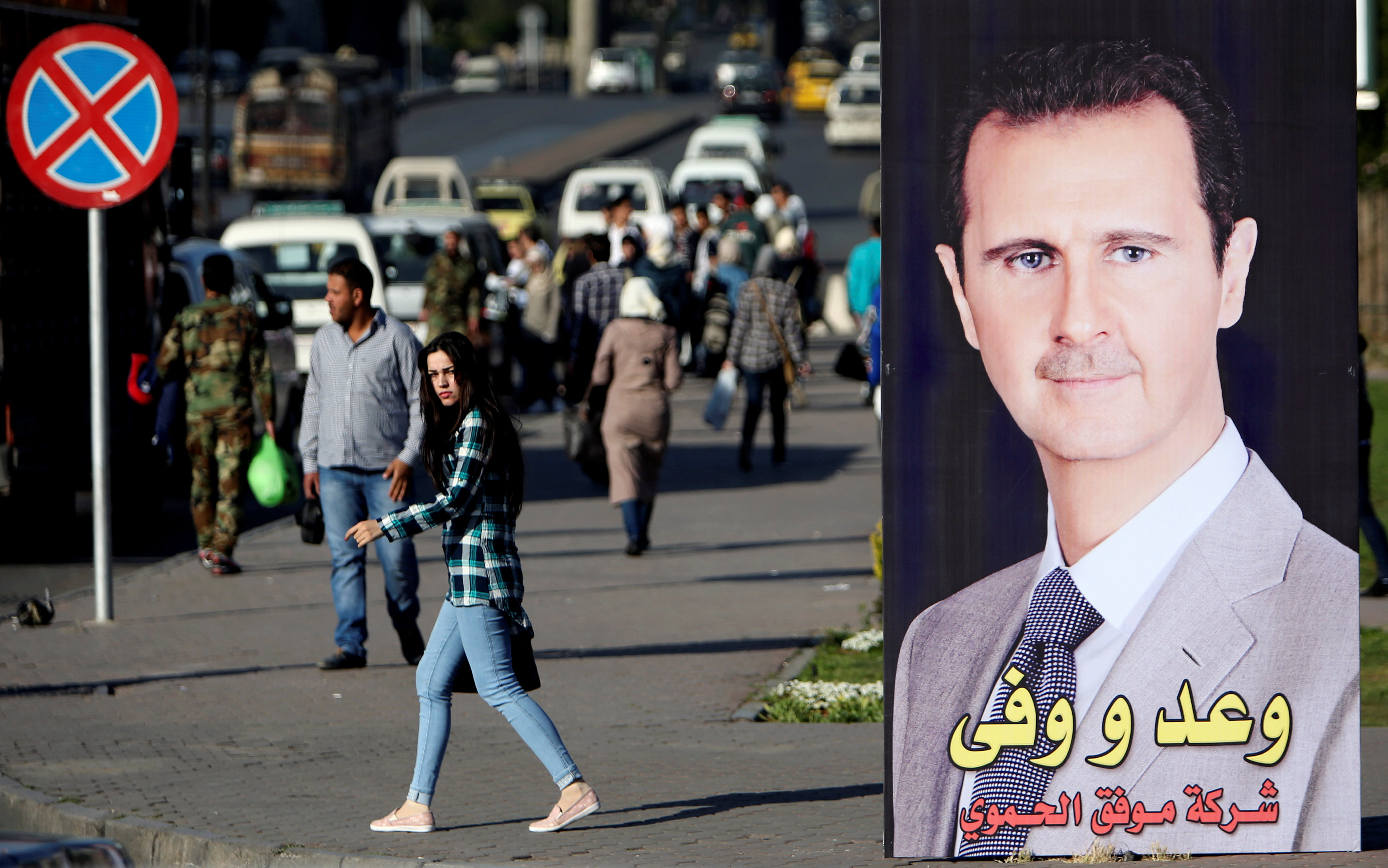 A woman walks near a picture of Syrian President Bashar al Assad in Damascus