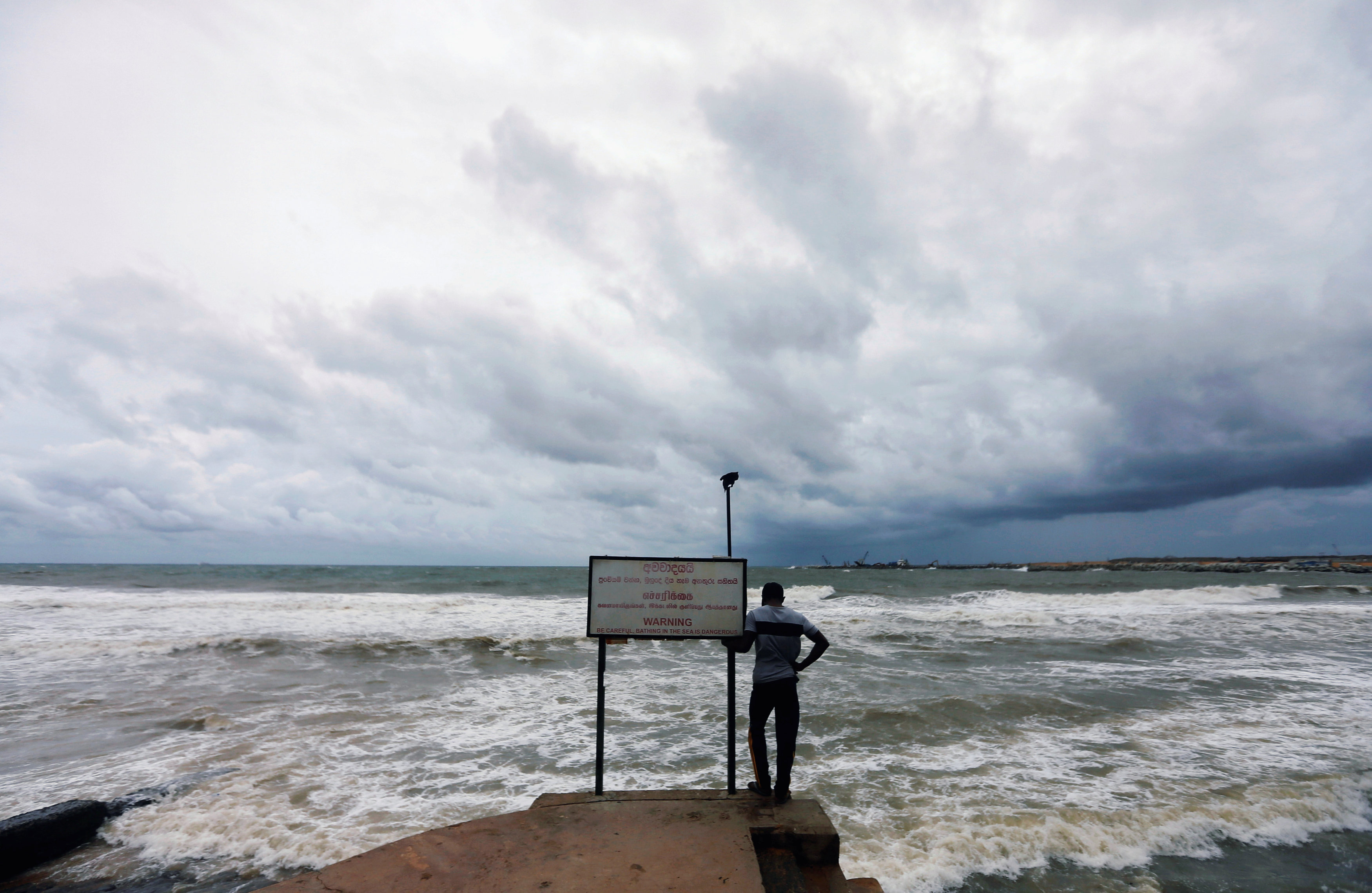 A man looks at the rough sea as rainy clouds gather above during the monsoon period in Colombo