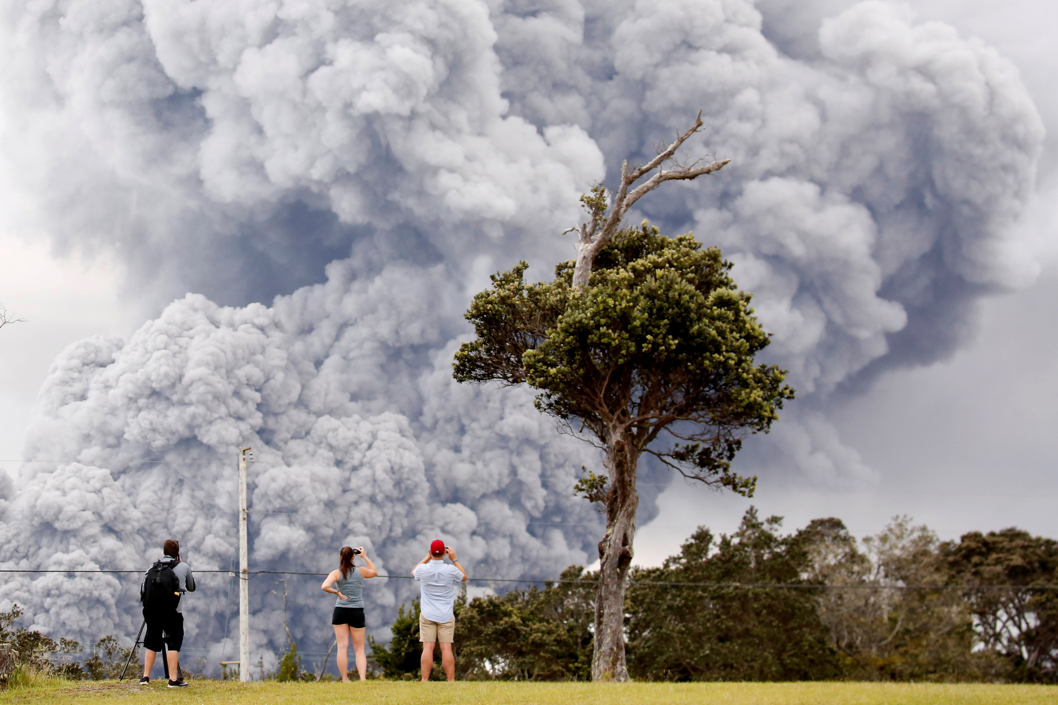 People watch as ash erupts from the Halemaumau crater near the community of Volcano