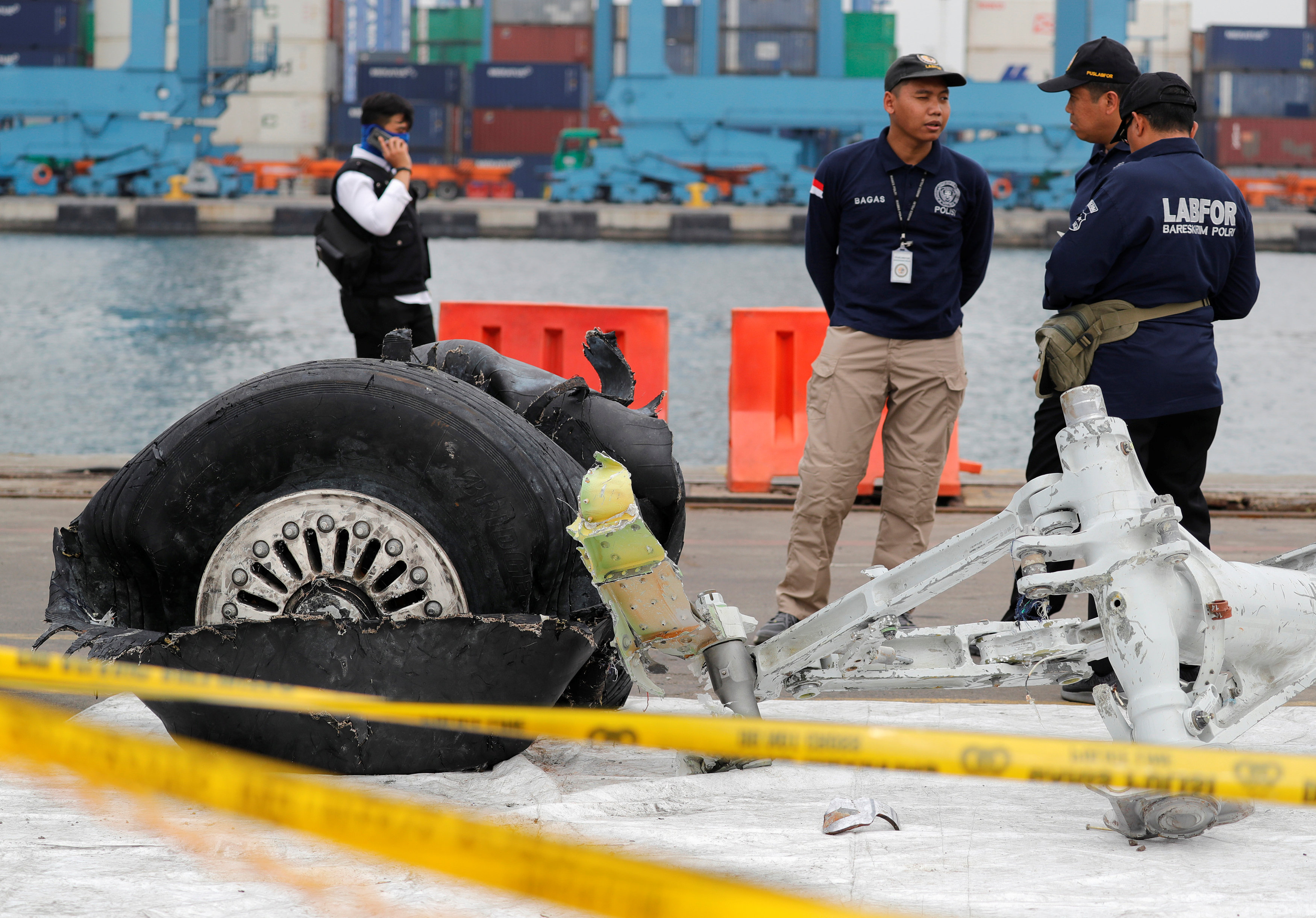 Indonesian forensic policemen stand beside a damaged tyre from the the Lion Air flight JT610 jet at Tanjung Priok port in Jakarta