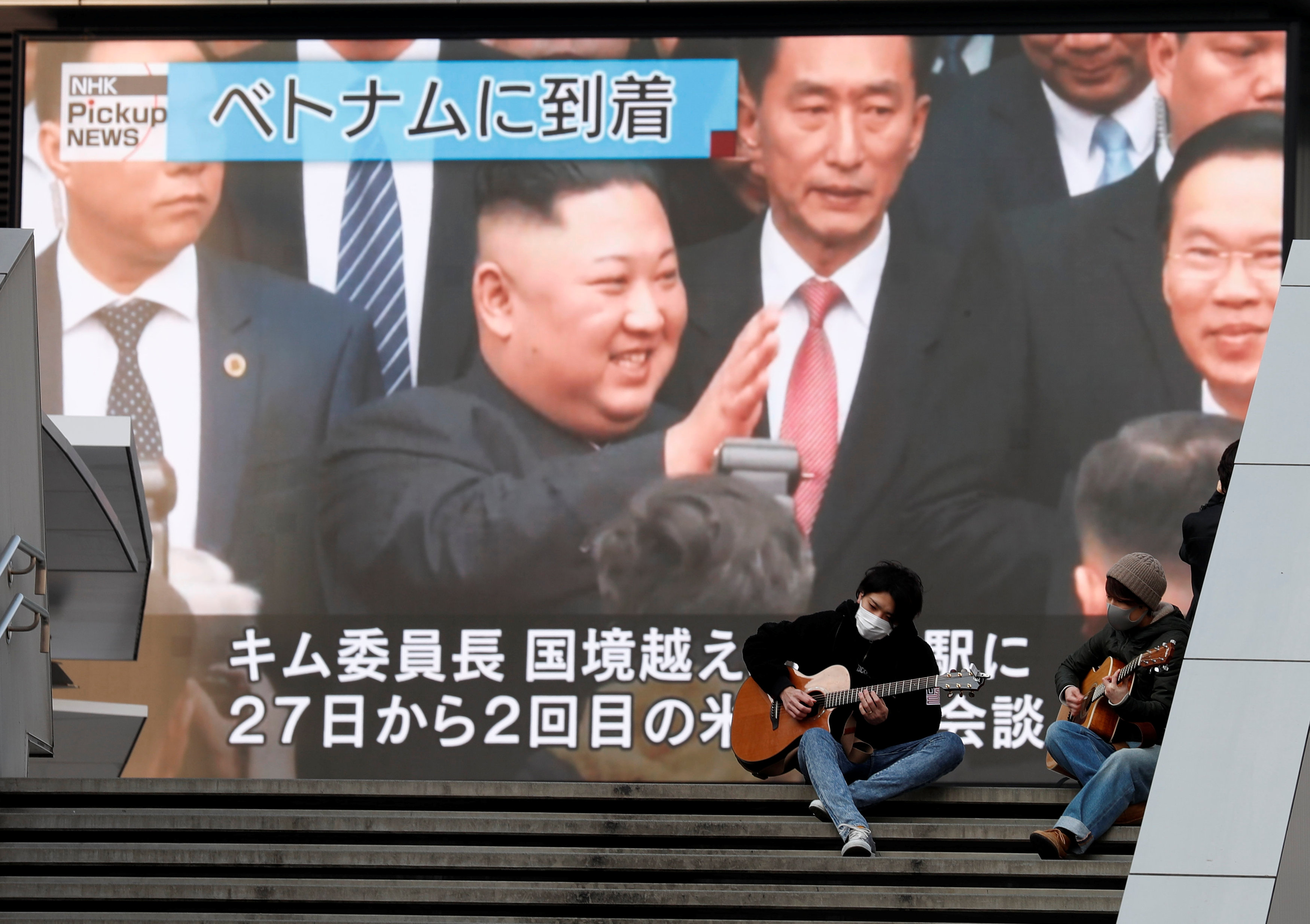 Men play guitars in front of a huge screen broadcasting North Korea's leader Kim Jong Un's arrival in Vietnam for the upcoming summit with U.S. President Donald Trump, in Tokyo