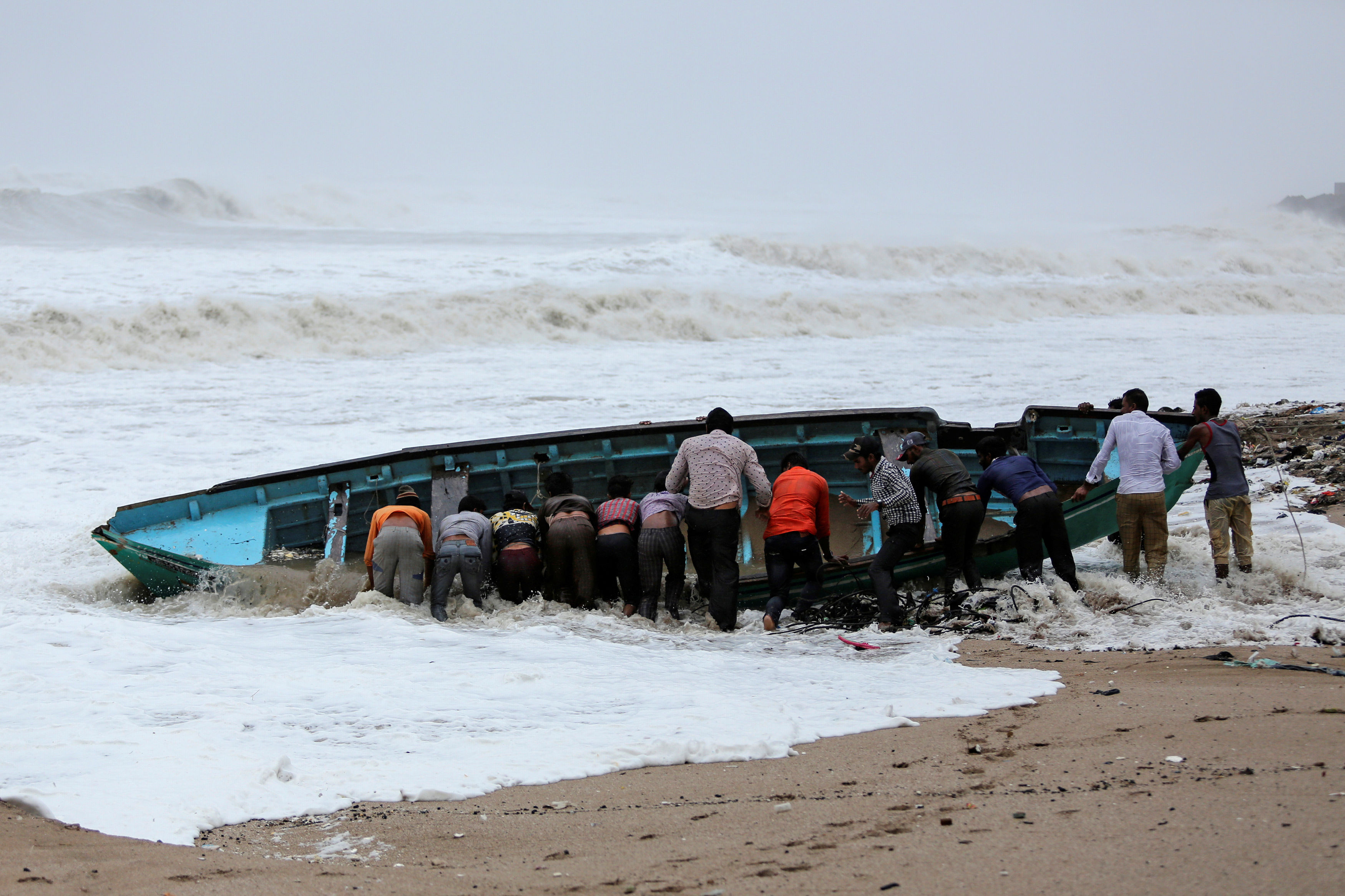 Fishermen move a fishing boat to a safer place along the shore ahead of Cyclone Vayu in Veraval