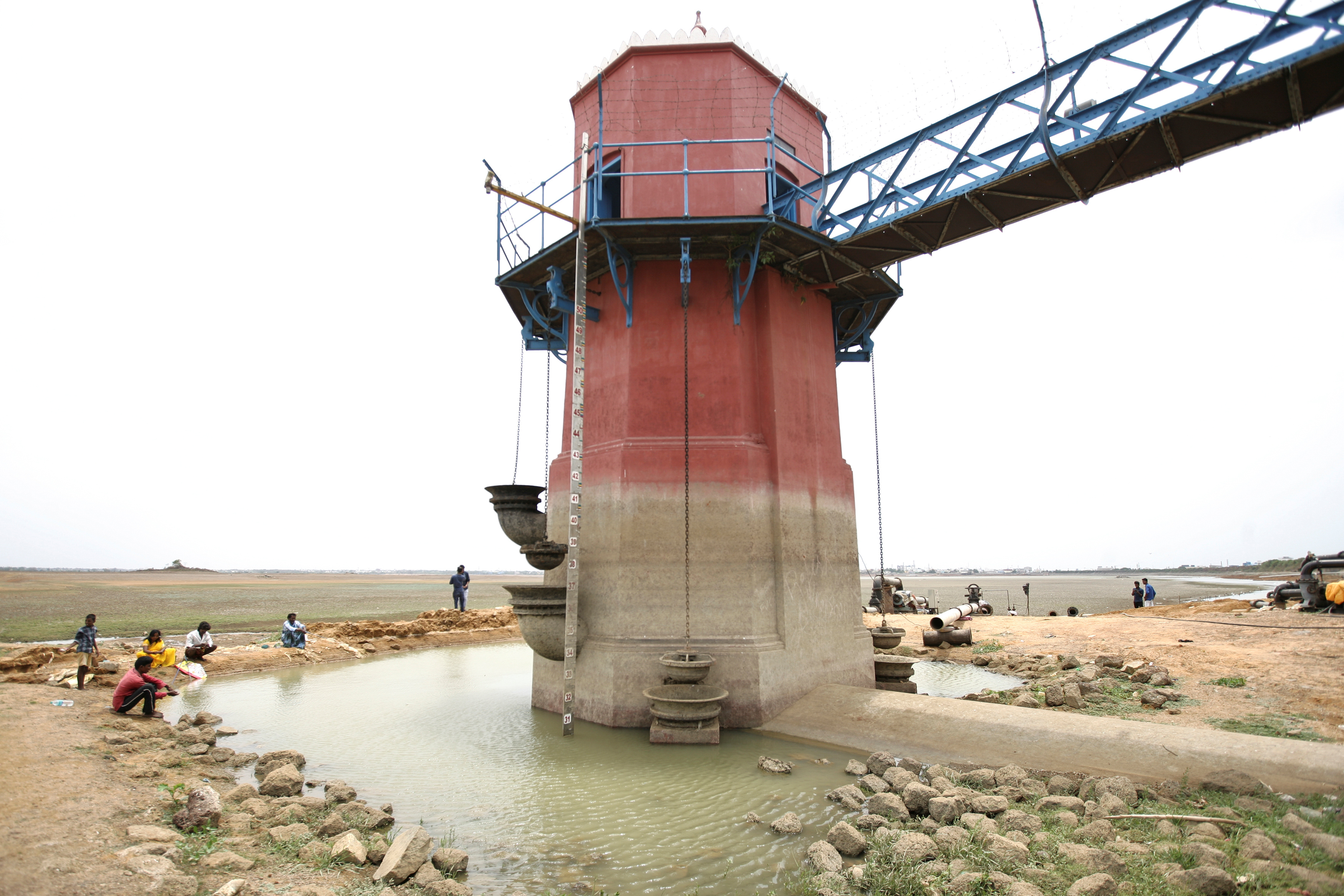 People sit around a tower for measuring water depth in the dried-up Puzhal reservoir, on the outskirts in Chennai
