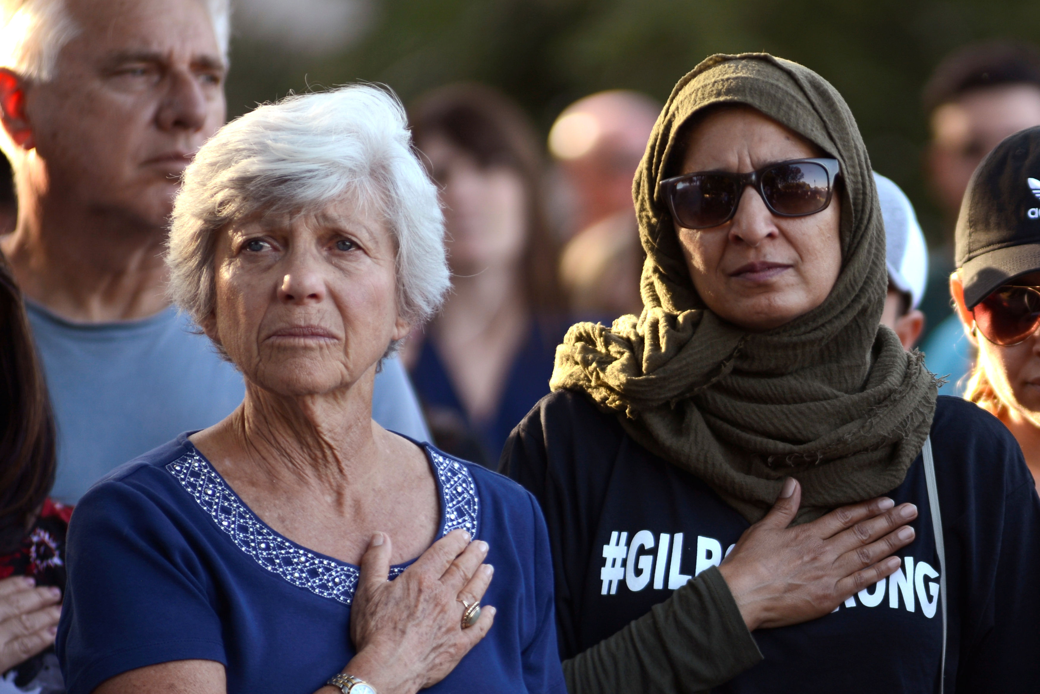 Women attend a vigil outside of Gilroy City Hall during the singing of the National Anthem honoring those that died and were injured during a mass shooting at the Gilroy Garlic Festival