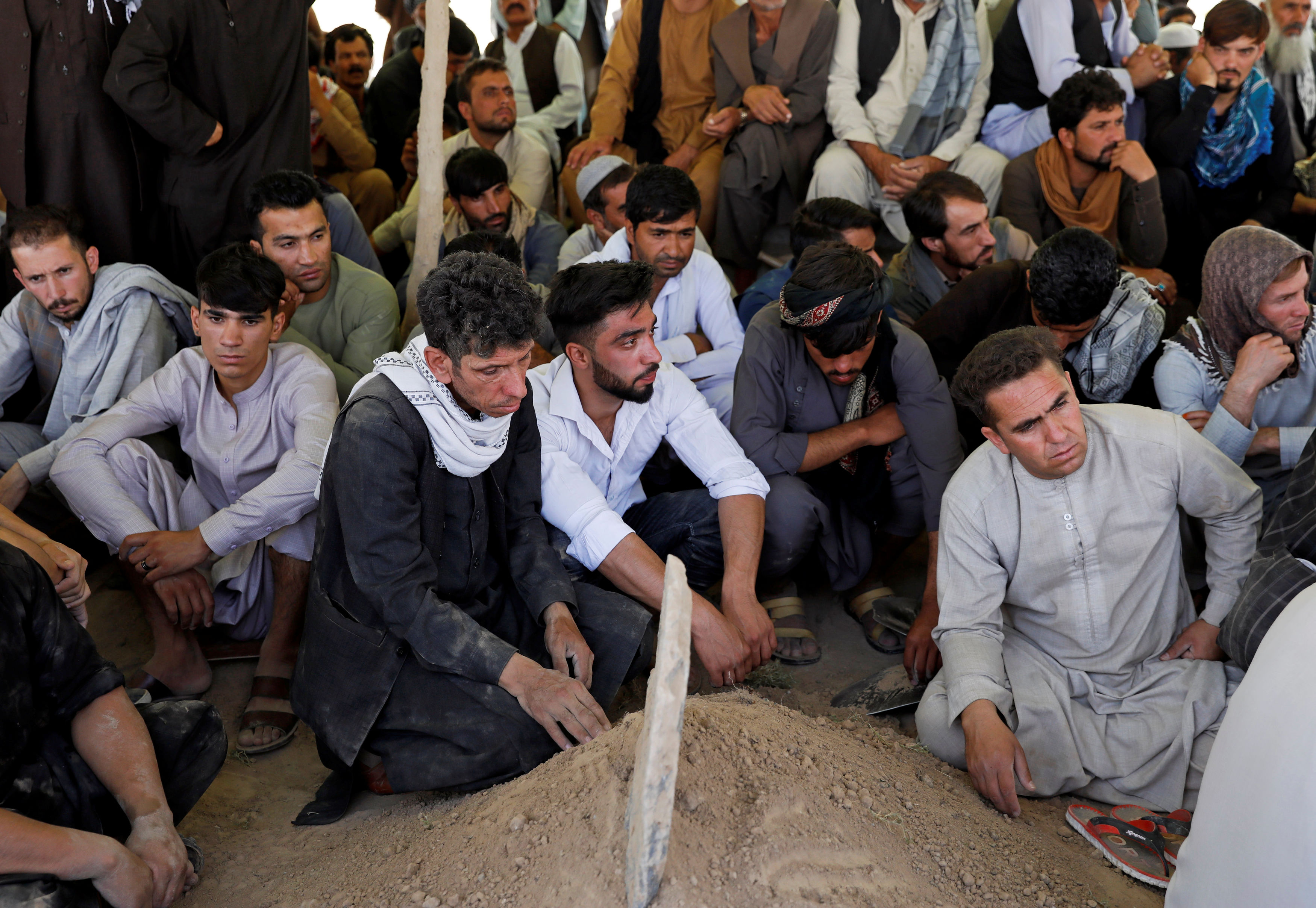 Afghan men attend the burial ceremony of the victims of a blast in a wedding in Kabul