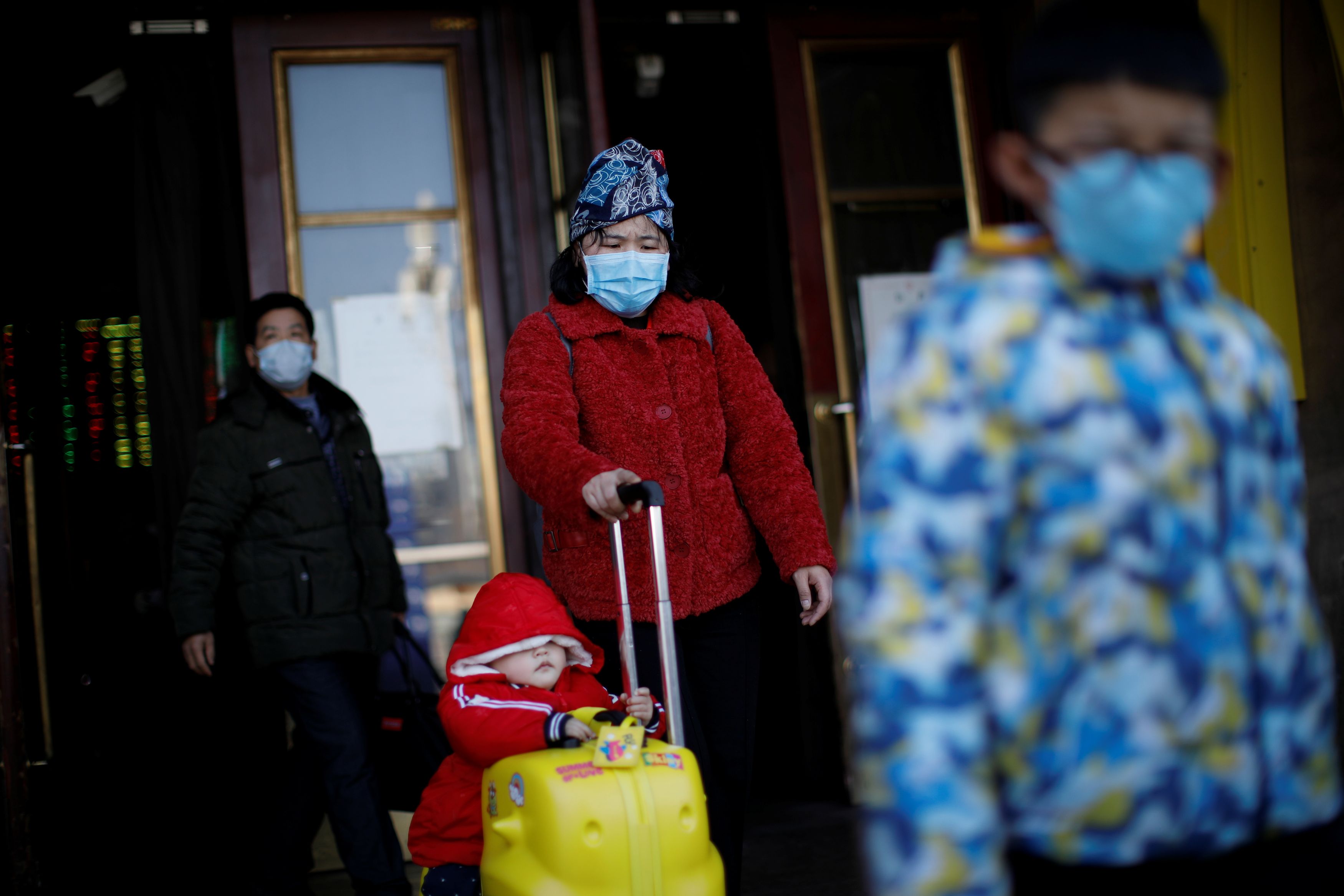 People wearing face masks carry their luggage as they walk outside Beijing Railway Station as the country is hit by an outbreak of the new coronavirus, in Beijing