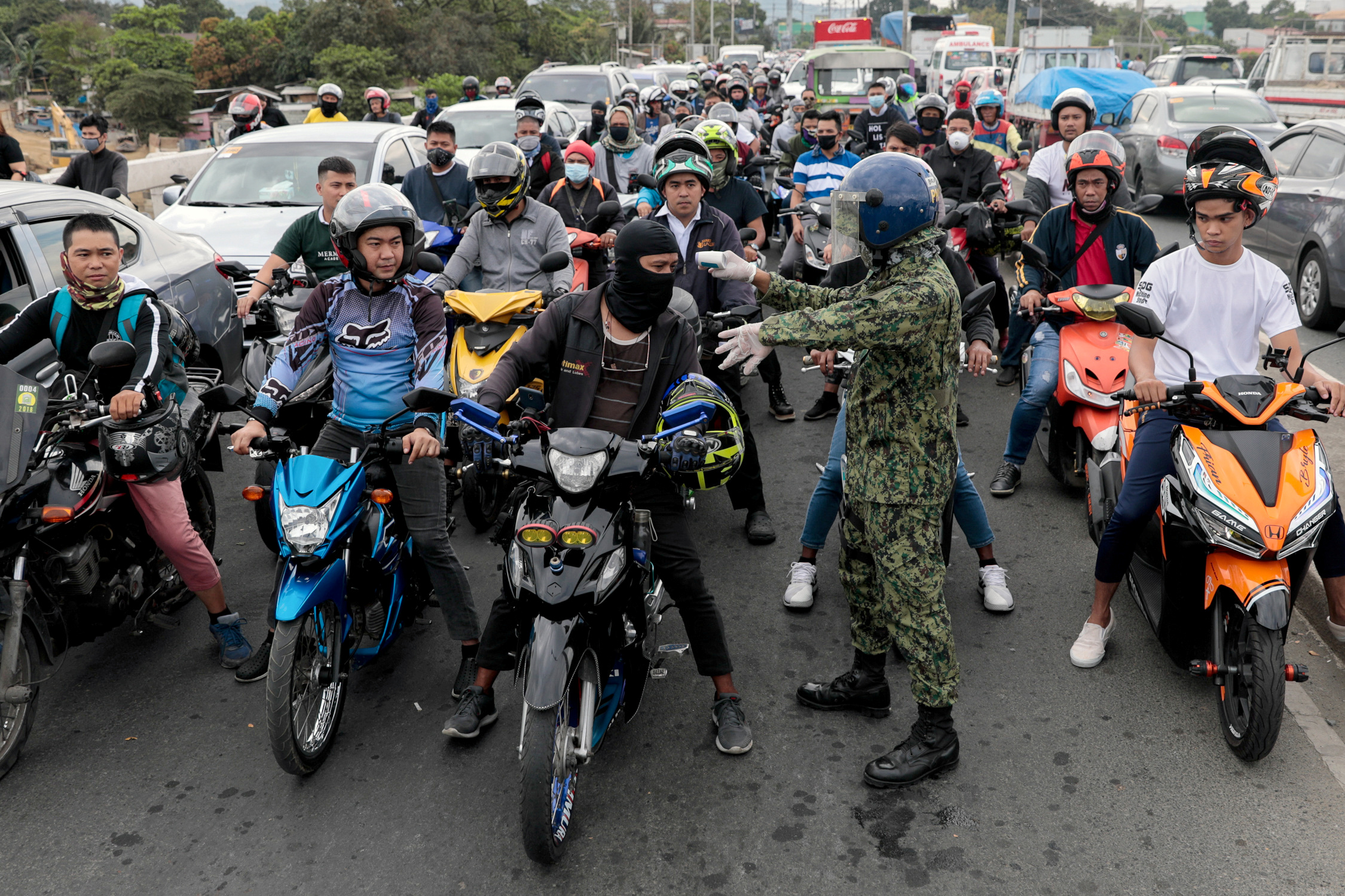 A police officer checks the body temperature motorists attempting to cross a checkpoint placed amidst the lockdown of the country's capital, to contain the spread of coronavirus, in the outskirts of Quezon City, Metro Manila